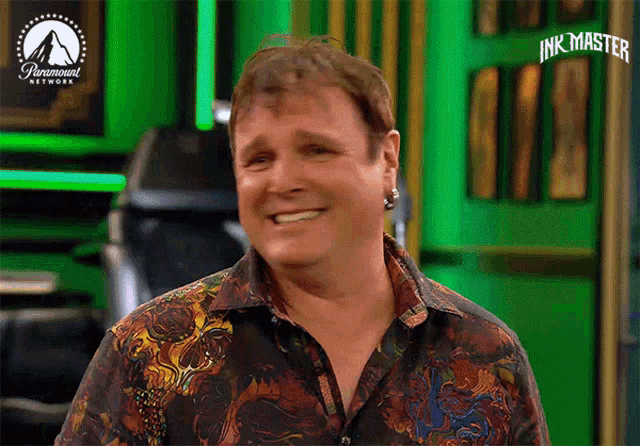 a man in a colorful shirt is smiling in front of a paramount network sign