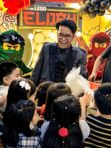 a man in a suit is surrounded by children in front of a sign that says the lego elijah