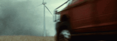 a red car is driving through a field with windmills in the background