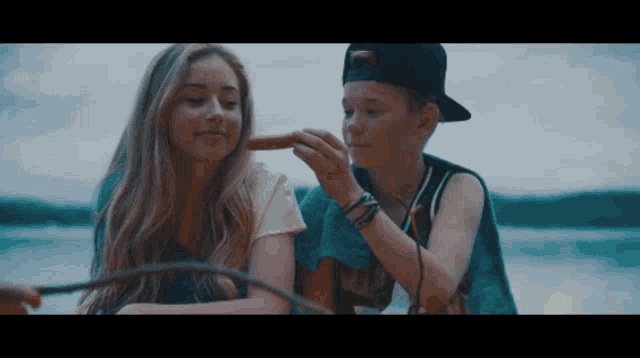 a boy is feeding a hot dog to a girl who is sitting next to him