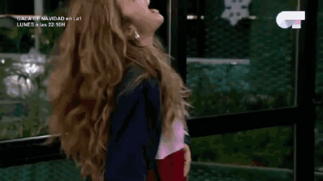 a woman with long blonde hair stands in front of a sign that says gala de navidad on it