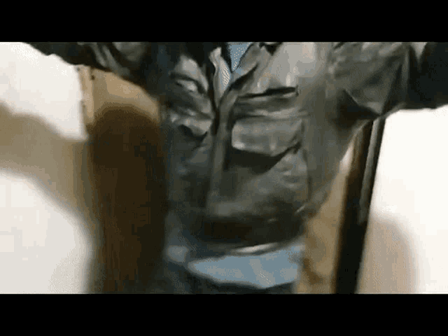 a man wearing a leather jacket and tie is standing in a room .