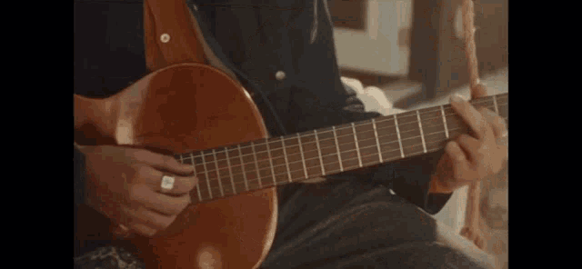 a man with a ring on his finger is playing an acoustic guitar .