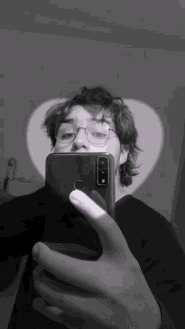 a man wearing glasses takes a selfie with a heart shaped light behind him