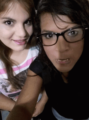 two girls are posing for a picture one wearing glasses