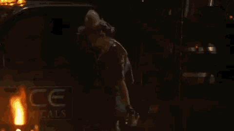 a woman is walking down a street at night in front of a burning trash can .