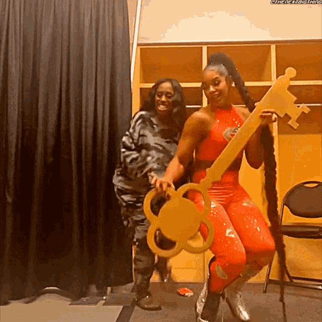 two women are posing for a picture in a locker room holding a large key .