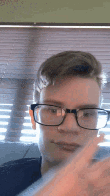 a young man wearing glasses is pointing to the camera