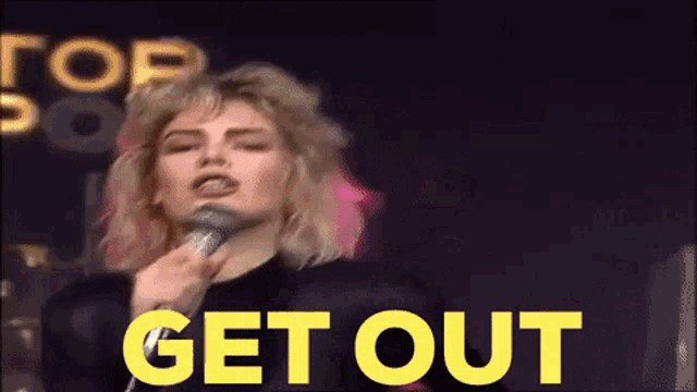 a woman singing into a microphone with the words get out in yellow letters