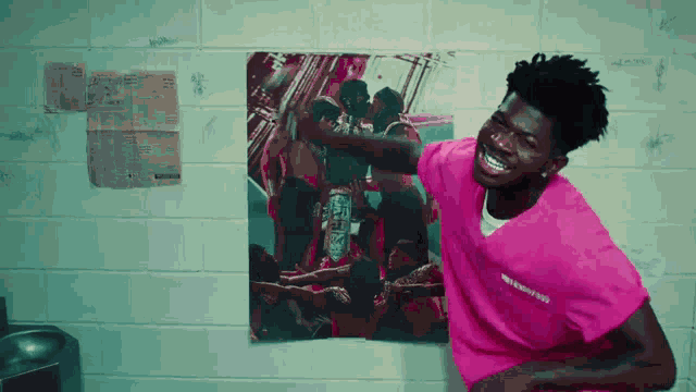 a man in a pink shirt is standing in front of a wall with a picture on it .