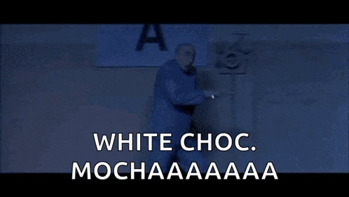 a man in a blue shirt is standing in front of a spotlight and says `` white choc . mochaaaa '' .