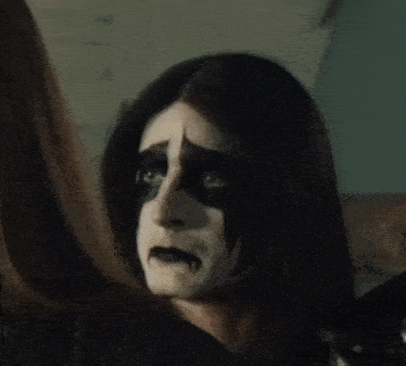 a woman with black and white paint on her face looks at herself in a mirror
