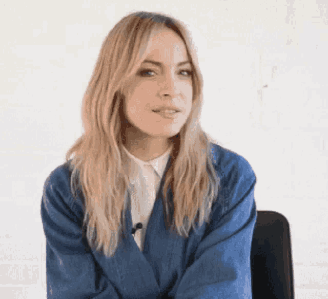a woman wearing a blue denim jacket and a white shirt is sitting in a chair .