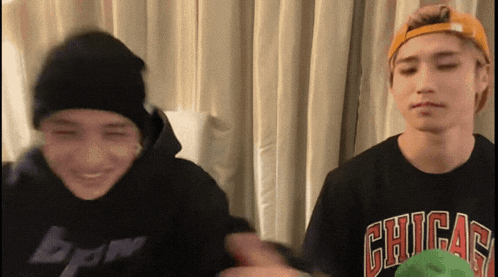 two young men are standing next to each other in front of a curtain and one of them is wearing a chicago shirt .