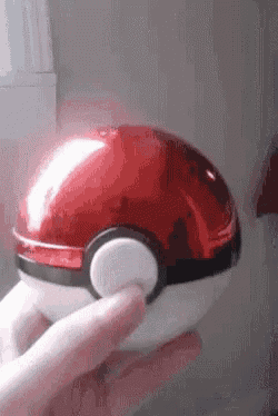 a person is holding a red pokeball in their hand .