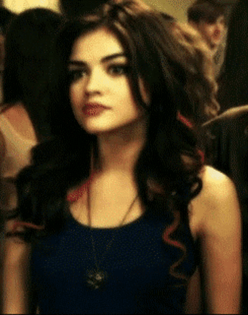 a woman wearing a blue tank top and a necklace looks to the side