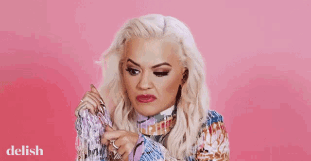 a woman with blonde hair is wearing a colorful sweater and making a face .