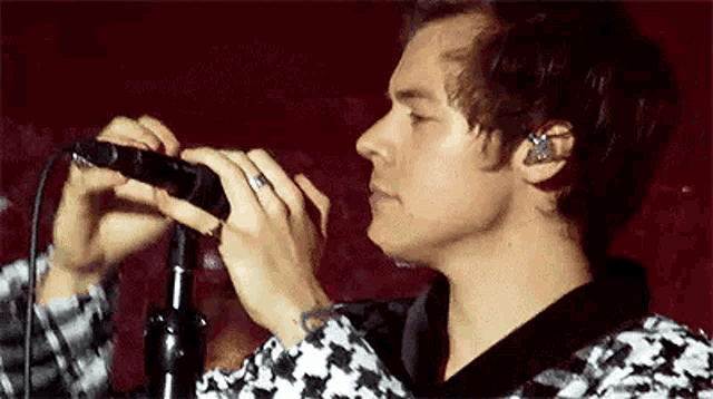 harry styles is holding a microphone in his hands while singing into it .