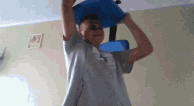 a boy is holding a blue bucket over his head in a room