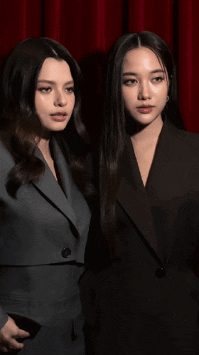 two women are standing next to each other wearing suits and looking at the camera