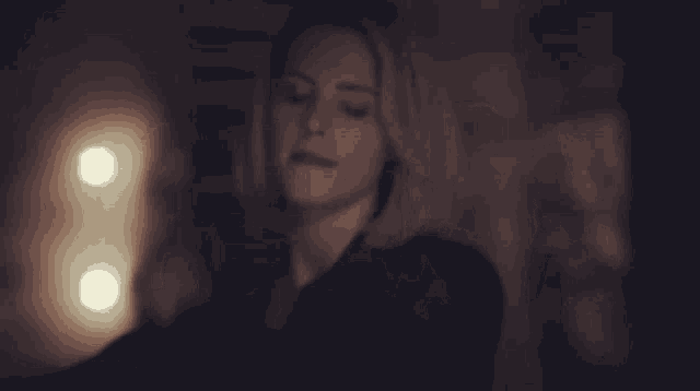 a woman is standing in a dark room with two lights behind her .