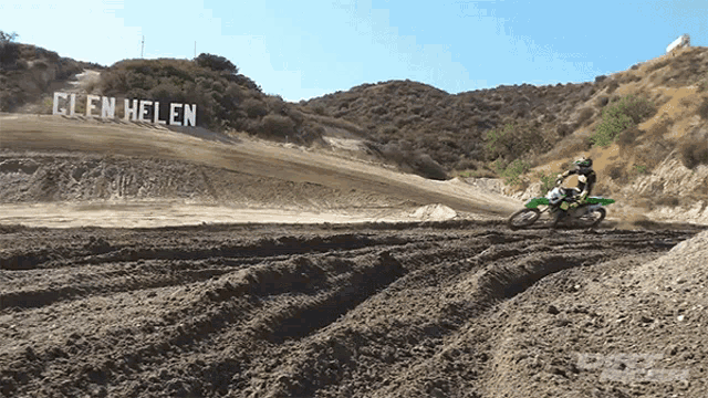 a person riding a dirt bike on a dirt track with a sign that says glen helen in the background