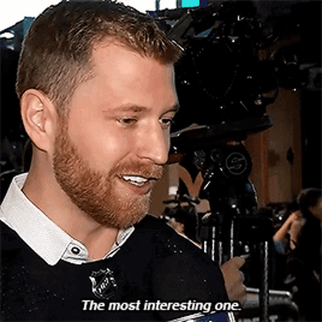 a man with a beard is talking into a microphone with the words " the most interesting one " below him