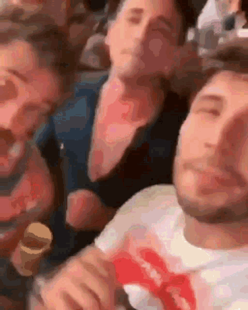 a man wearing a rolling stones shirt is sitting in a crowd of people .