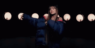 ariana grande is wearing a blue puffer jacket and dancing in front of a group of lights .