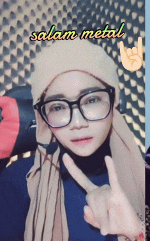 a woman wearing glasses and a beanie is giving a peace sign in front of a wall that says salam metal