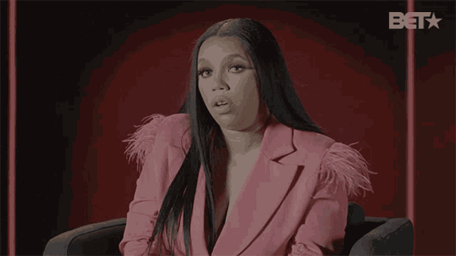 a woman wearing a pink jacket with feathers on the sleeves is sitting in front of a bet logo