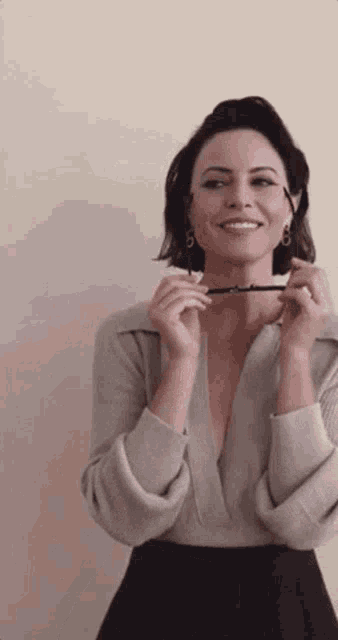 a woman wearing a sweater and earrings is holding a pair of glasses in front of her face .