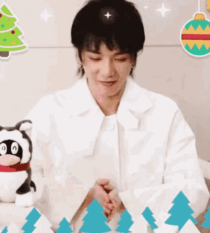 a man in a white shirt is sitting at a table with a stuffed animal and a christmas tree in the background .