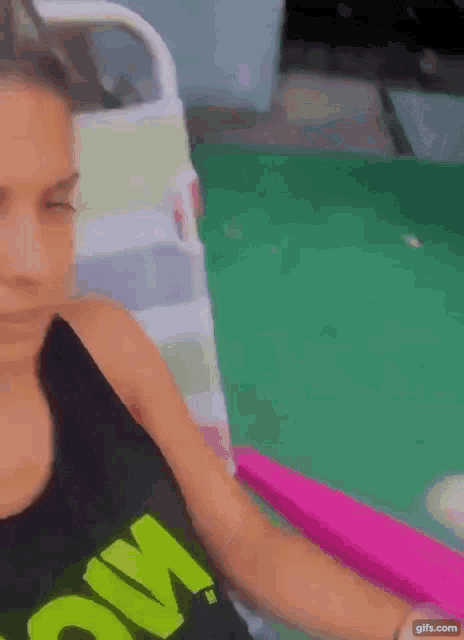 a woman in a black tank top is sitting in a pink chair next to a pool .