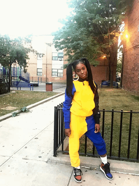 a girl wearing a yellow and blue outfit is leaning on a fence