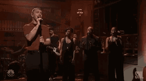 a man singing into a microphone in front of a group of people with snl written on the bottom