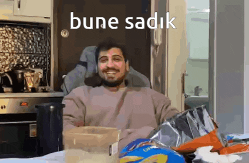 a man is sitting in a chair in a kitchen with a bag of chips and a box of chips .