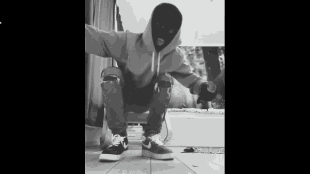 a man wearing a ski mask and a hoodie is squatting down