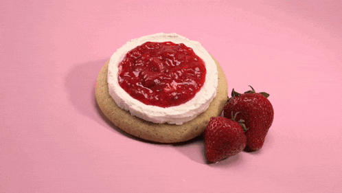 two strawberries are sitting on top of a cake with whipped cream on a pink surface .