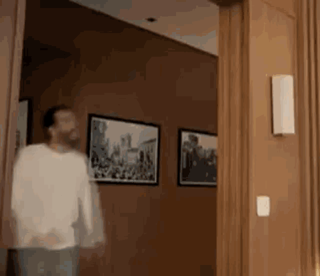 a man in a white shirt is walking through a doorway in a room .
