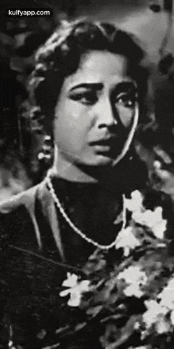 a black and white photo of a woman wearing a pearl necklace holding a bouquet of flowers .