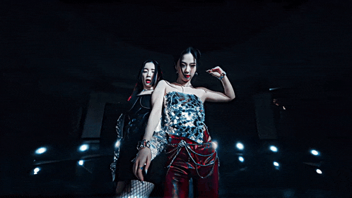 two women are posing for a picture in a dark room with lights behind them