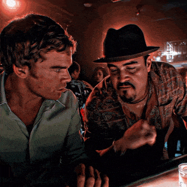 a man in a hat talks to another man in a green shirt