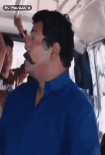 a man with a mustache is sitting on a bus and looking at the camera .