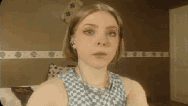 a young woman wearing headphones and a checkered shirt is sitting on a bed .