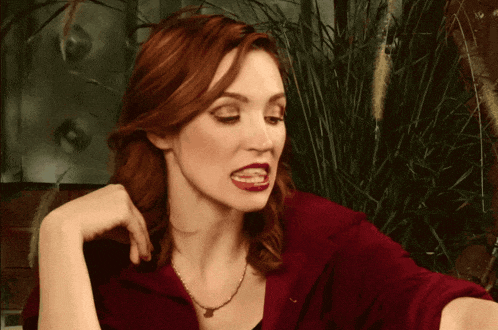 a woman with red hair is wearing a red shirt and a gold necklace