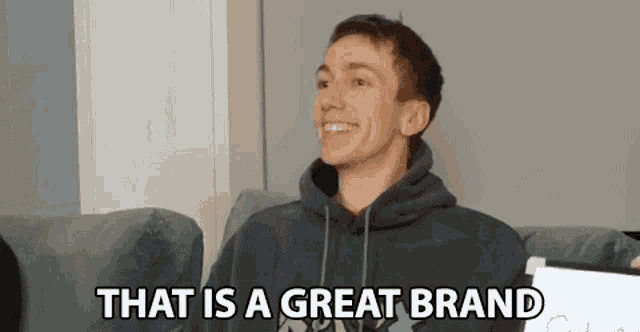 a young man in a hoodie is sitting on a couch and smiling .