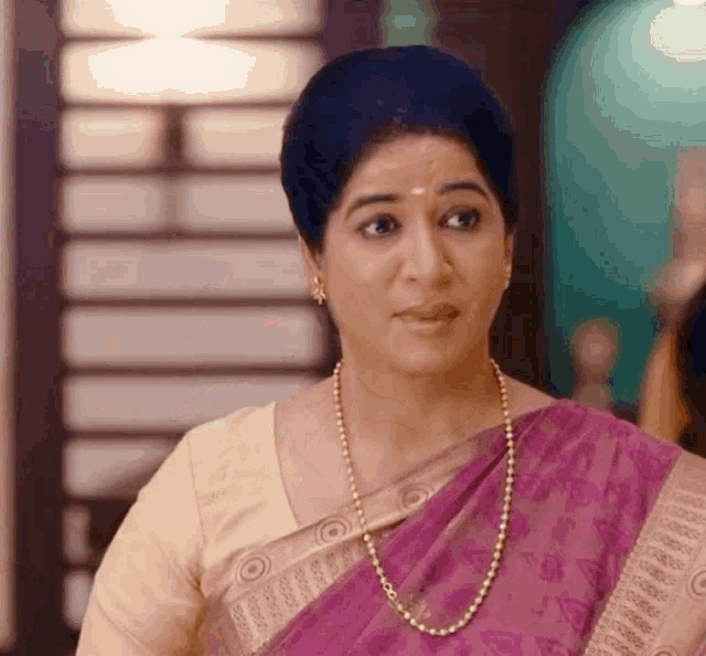 a woman wearing a purple saree and a pearl necklace is looking at the camera .