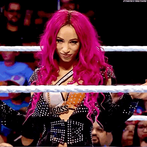 a woman with pink hair is standing in a wrestling ring wearing a necklace that says boss .