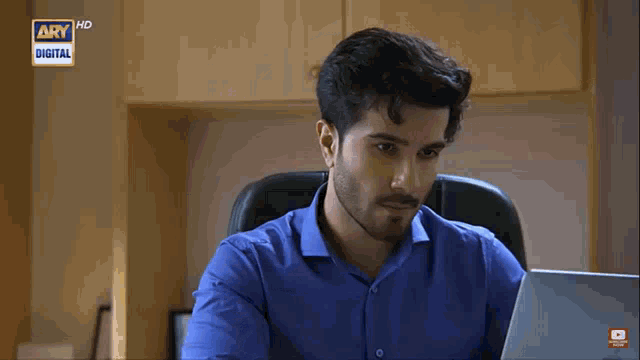 a man in a blue shirt is sitting in front of a laptop with ary digital on the screen